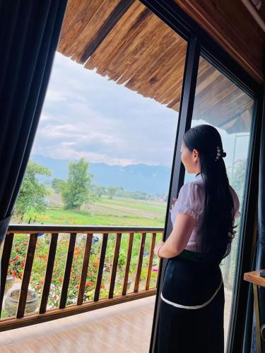 a woman standing on a balcony looking out of a window at Trần Gia Homestay in Văn Chấn