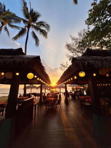 a restaurant on the beach with a sunset in the background at Nang Thong Beach Resort in Khao Lak