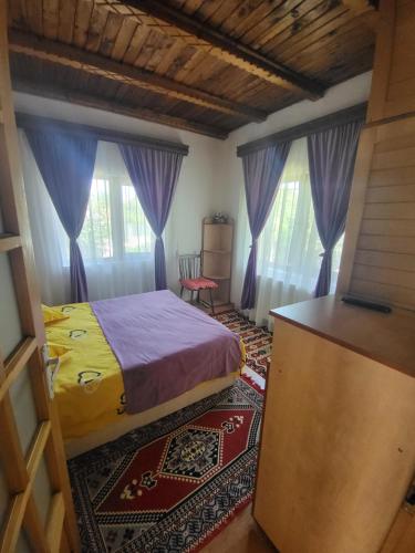 a bedroom with a bed and two windows with purple curtains at Casa Roza in Breaza de Sus