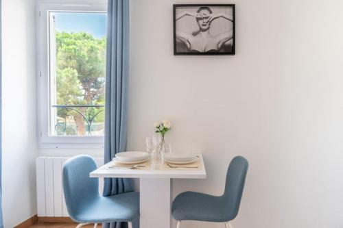 une table blanche avec des chaises bleues et une fenêtre dans l'établissement Confortable appartement - Cannes centre le Suquet, à Cannes