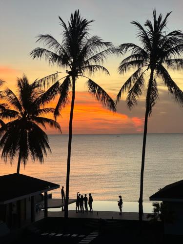 a group of people walking on a beach with palm trees at Reboot Retreat Beach Resort, Restaurant, and Coffee Shop in Ban Talat Bang San