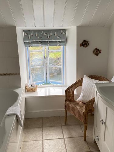 a bathroom with a tub and a window and a chair at Lugger Hotel ‘A Bespoke Hotel’ in Portloe