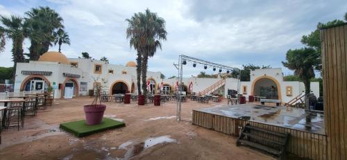 un patio avec tables, chaises et palmiers dans l'établissement Mobil home - Camping La Palmeraie, à Torreilles