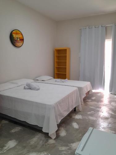 two beds in a white room with a window at Pousada Flor da Barra in Maragogi