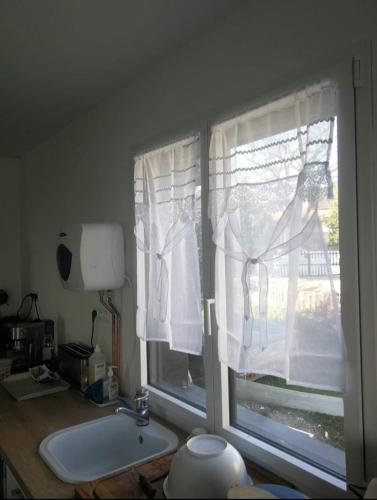 La salle de bains est pourvue d'une fenêtre avec des rideaux blancs et un lavabo. dans l'établissement Chez Muriel et Elain, à Culmont
