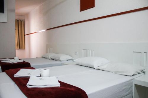 Dos camas en una habitación con sábanas y toallas blancas. en Hotel Itaquera, en São Paulo