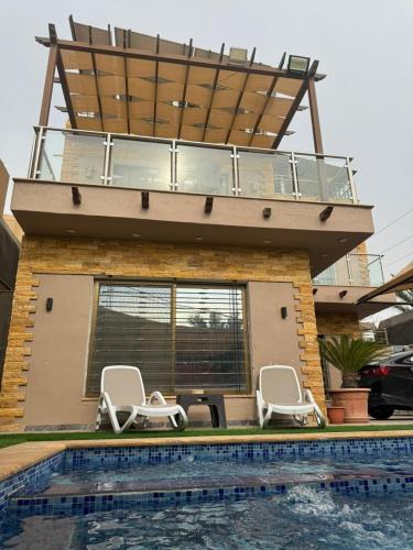 a house with a balcony with chairs and a pool at Yasmina Chalet in Al Kafrayn