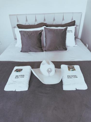 a bed with three pillows and a hat on it at Hotel Rosa Viva in Barretos
