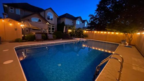 a swimming pool with lights in a backyard at night at Metropolitan Dream Stay with Saltwater Pool and Hot Tub in Surrey