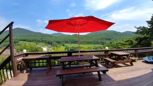 a picnic table with a red umbrella on a deck at Another world pension in Gyeongju