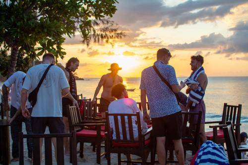 a group of people standing on the beach watching the sunset at Amara Beach Resort Koh Phangan in Haad Yao