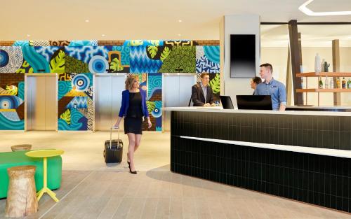a woman with a suitcase walking past a counter at Holiday Inn Express Adelaide City Centre by IHG in Adelaide