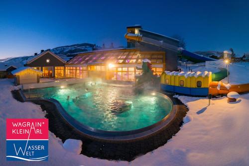 a house with a swimming pool in the snow at Goldhirsch Aparthotel in Wagrain