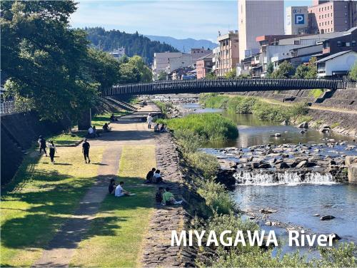 a group of people sitting on the grass near a river at Backpackers Hida Takayama in Takayama