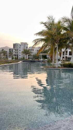 a large swimming pool with palm trees and buildings at 2BHK furnished flat with jacuzzi in As Sīfah