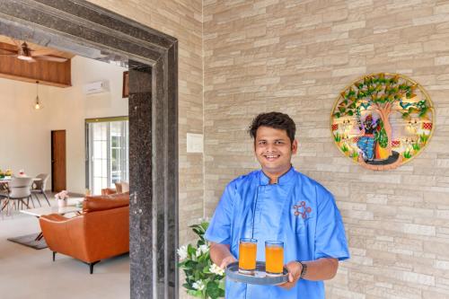a man holding a tray of orange juice at SaffronStays Riverdeck Vista in Karjat