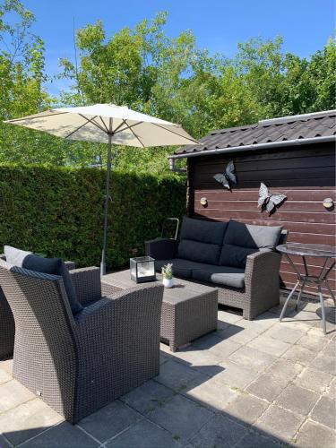 un patio con due divani e un ombrellone di Verzorgd chalet in de Betuwe op park met natuurbad a Beesd