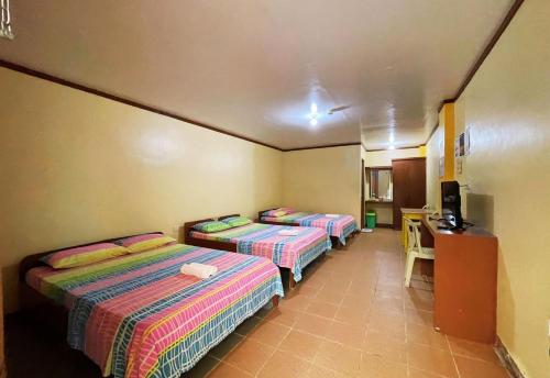a room with three beds and a desk and a television at White Beach Hotel Puerto Galera powered by Cocotel in Puerto Galera