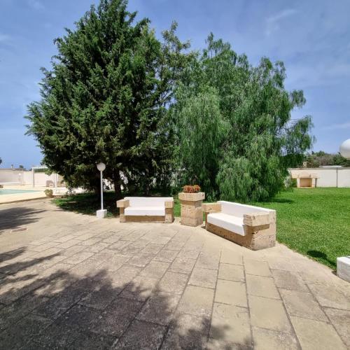 two benches sitting in a park next to a tree at Villa Dei Lidi - HomeSalento com in Torre San Giovanni Ugento
