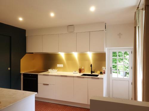 une cuisine avec des placards blancs et un mur jaune dans l'établissement Gîte de charme XIXe, à Grand-Champ