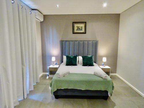 a bedroom with a bed with green pillows and curtains at The Executive - Exclusive Self-Catering Apartments - Ezulwini in Ezulwini