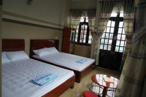 two beds in a room with two tables and windows at Thanh Lich Guesthouse in Quảng Ngãi