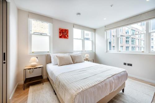 a white bedroom with a bed and two windows at Two Bed Duplex in Covent Garden in London