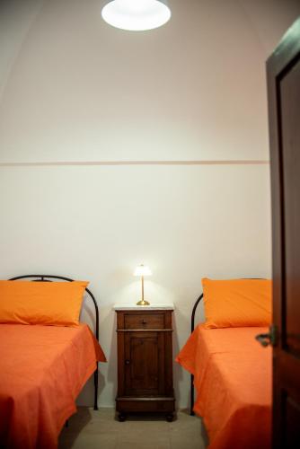 two beds with orange pillows and a table with a lamp at I Trulli e la Luna in Alberobello