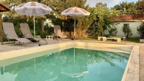 a swimming pool with two chairs and two umbrellas at Tiszaháló Apartman Ház in Kisköre