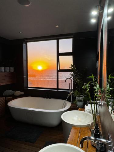 a bath tub in a bathroom with a view of the sunset at Beachfront Luxury Oasis in Rand Rifles