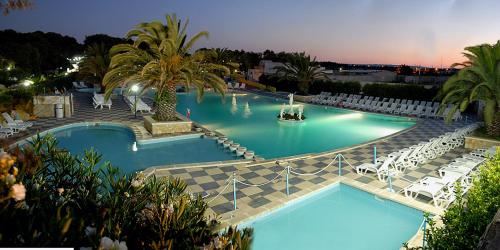 una gran piscina con sillas blancas en un complejo en Camping Villaggio Pineta Al Mare, en Specchiolla