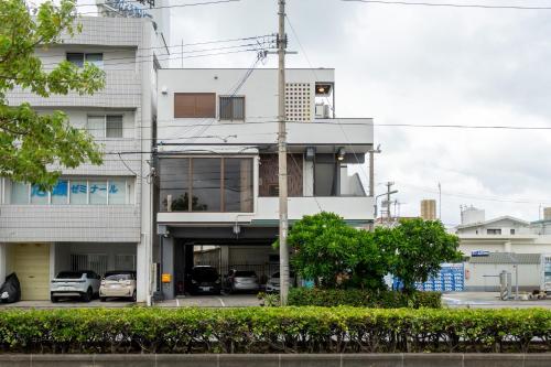 a white building with cars parked in a parking lot at アワセベイストリートホテル in Okinawa City