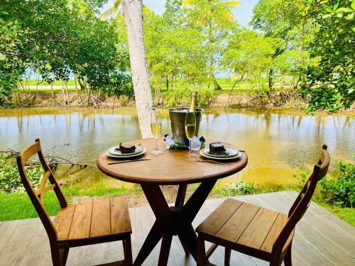 a wooden table with two chairs next to a river at Angá Beach Hotel in São Miguel dos Milagres
