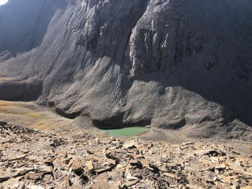 a mountain with a green lake in the middle at La Chaumière, Formule maison entière in Colmars
