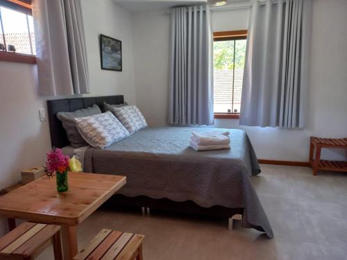 a bedroom with a bed and a table and windows at Encanto da Serra Suítes Lumiar in Lumiar