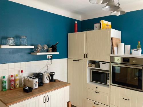 une cuisine avec des armoires blanches et un mur bleu dans l'établissement Maison lumineuse, à Bagnols-sur-Cèze