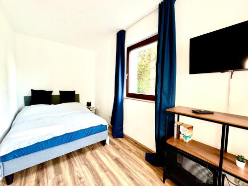a bedroom with a bed with blue curtains and a television at Chices Service Apartment nahe Homburger Uni Klinik und Technologiepark mit Loggia und kostenlosem Parkplatz in Homburg