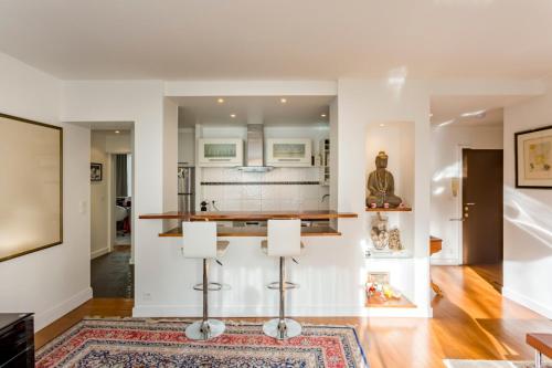 une cuisine aux murs blancs et un bar avec tabourets dans l'établissement Calme dans la verdure Paris 16e, à Paris