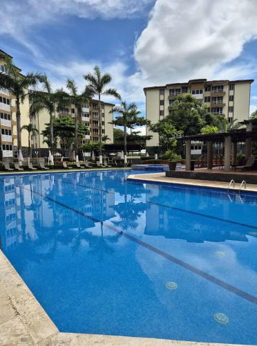 a large blue swimming pool with buildings in the background at Family getaway, pool, beach and surf in Jacó