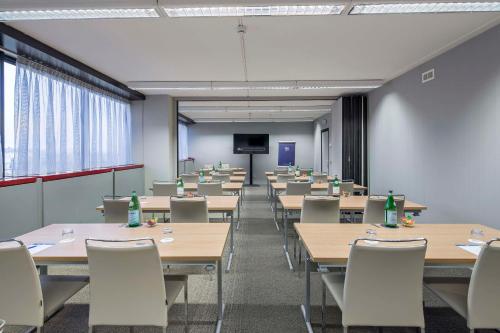 a classroom with tables and chairs and a screen at NH Milano Congress Centre in Assago