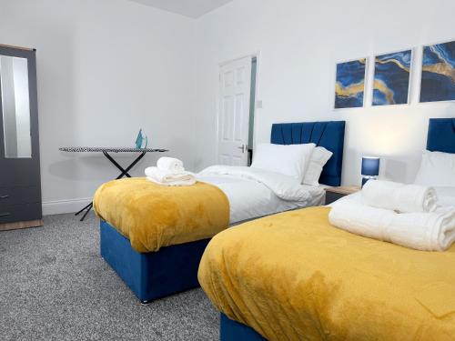 a bedroom with two beds with yellow sheets and a table at Hampton Blues 3BR Entire Home in Stockton-on-Tees