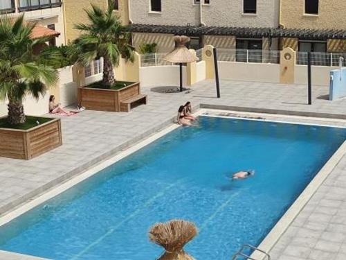 une grande piscine bleue avec des personnes assises autour de celle-ci dans l'établissement Duplex T4 Confort 6 Pers., Piscine, Parking, Centre Port à Gruissan - FR-1-796-74, à Gruissan