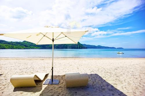a beach with two chairs and an umbrella on the sand at PICO DE LORO Beach Walking Distance MIRANDA 1 Bedroom Units by SEE Condominiums in Cutad