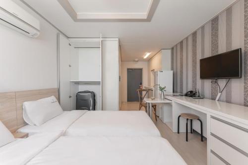 a bedroom with two beds and a desk with a television at Staywell Hotel in Busan