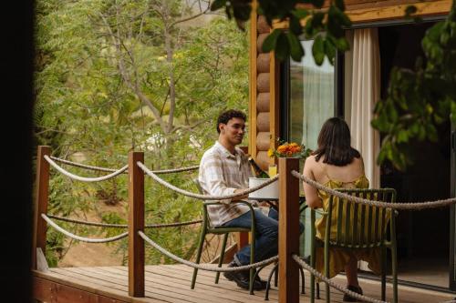 a man and a woman sitting at a table on a porch at Boskenvid Hotel - Romantic Treehouses & Skypool in Valle de Guadalupe