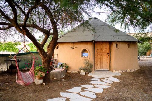 a small house with a tree and a hammock in front of it at ביתהבוצ - מקום טבעי למפגשים in Talmei Yosef