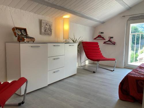a bedroom with a red chair and white cabinets at Maison bord de rivière in Roquestéron