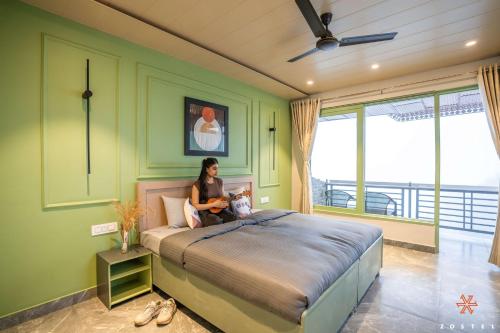 a woman sitting on a bed in a room with green walls at Zostel Dharamkot in McLeod Ganj