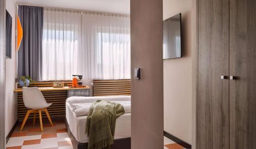 a bedroom with a bed and a desk and a window at Flemings Hotel München-Schwabing in Munich