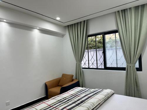 een slaapkamer met een bed, een stoel en een raam bij Masaki-2Bedroom-G03 in Dar es Salaam